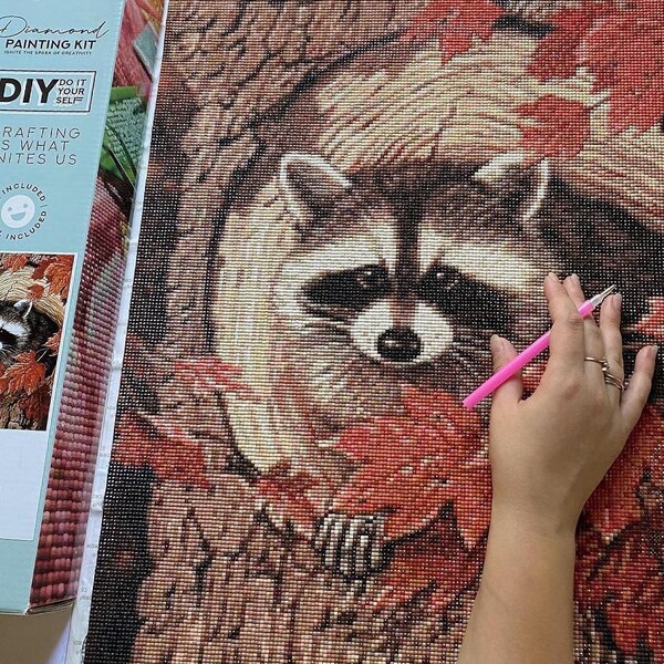 hand completing diamond art painting of raccoon